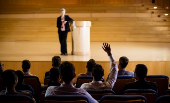 A man raising his hand to ask a question from a conference speaker.