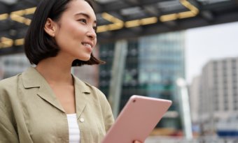Asian woman holding a tablet outside with buildings in the background